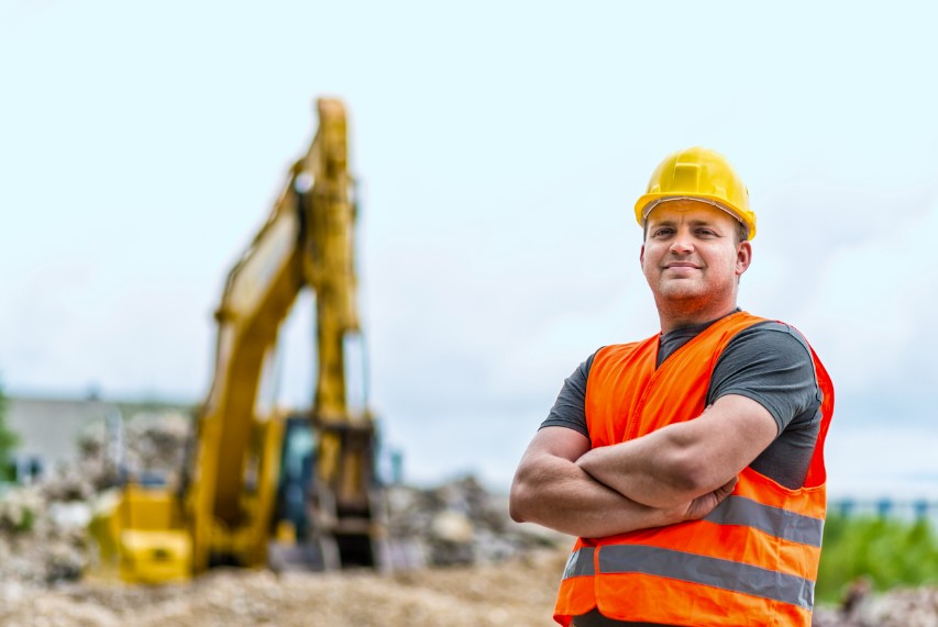 Portrait of a male excavator driver with the excavator and dirt in the background.